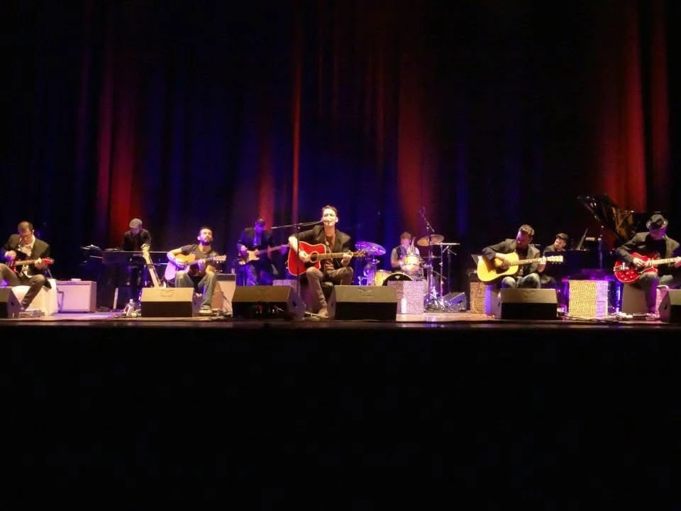 Lo spettacolo in teatro con musicisti seduti e chitarre acustiche